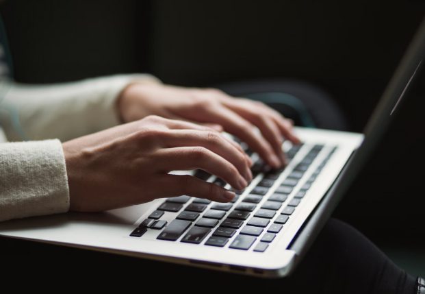Close up of woman's hands typing on a laptop keyboard while sitting down.