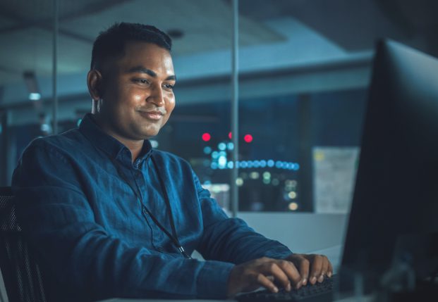 Technology expert working at night in the office with servers in the background.