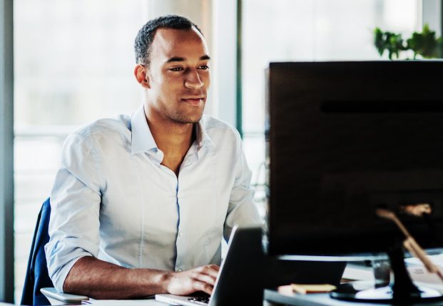 Business person in office looking at computer screen typing out information.