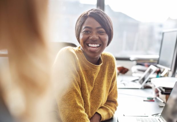 Woman smiling at another co-worker sitting in front of desk