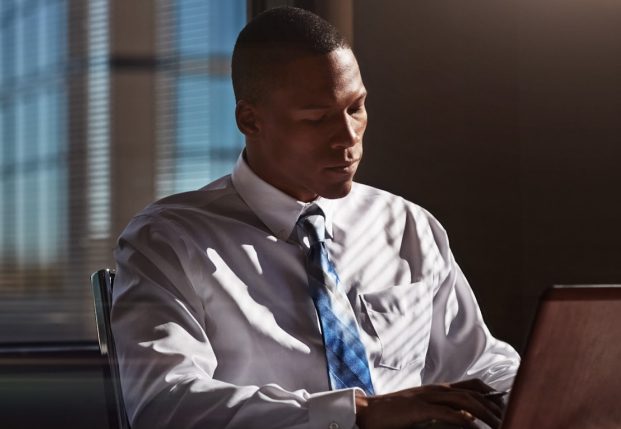 Business man with white shirt and tie sitting at night time in the office and working on computer.