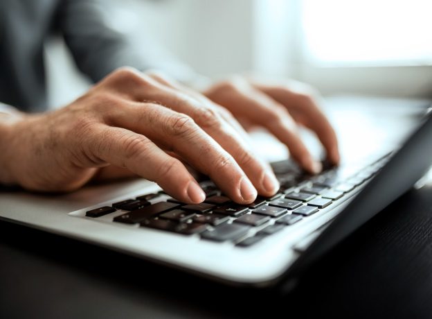 Close up of mans hands typing on keyboard while working in the office.