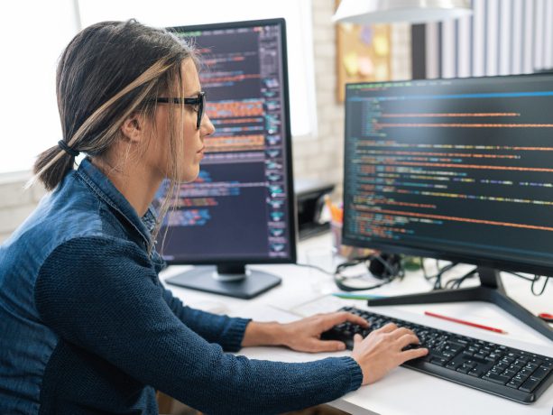 Female developer working at desk writing code on screen.