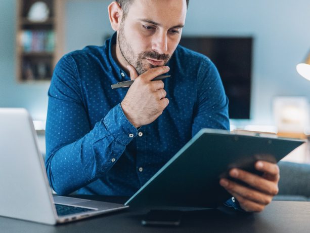 Business person at home holding a pen and clipboard reviewing notes.